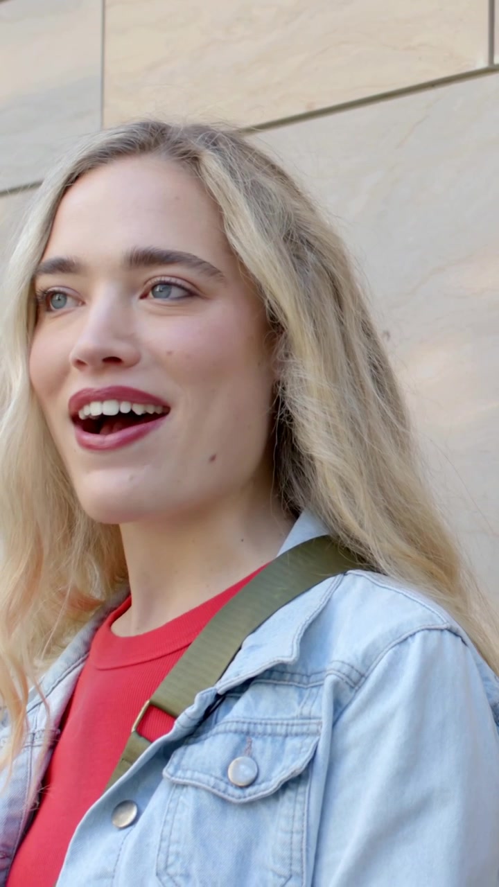 Video verticale: Donna che risponde al partner che parla, donna in denim che sorride vicino a una parete piastrellata, spallina verde.