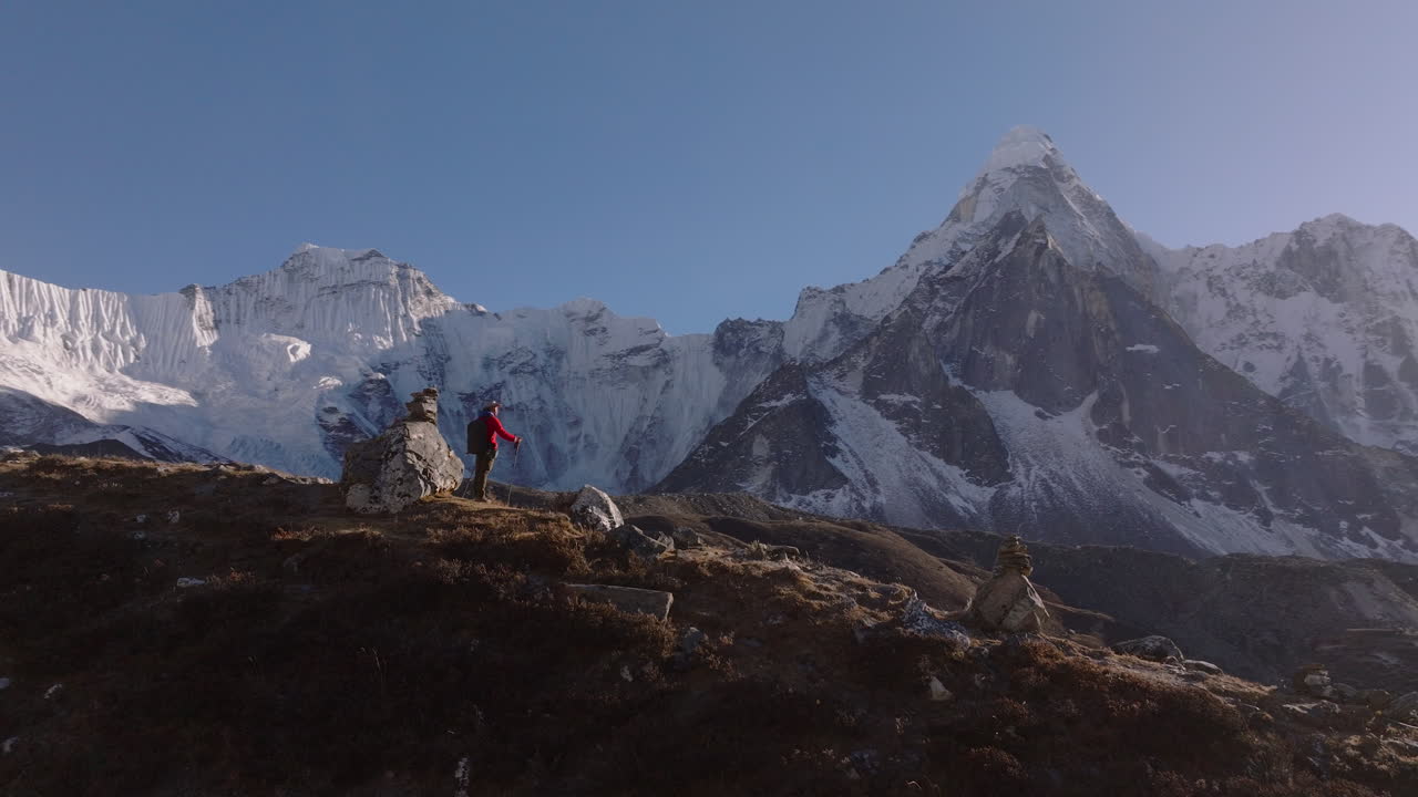Evening drone shot of a tourist pausing on Nepal’s Everest Base Camp trekking route to take in the Himalayan surroundings. Ama Dablam stands prominently in the background