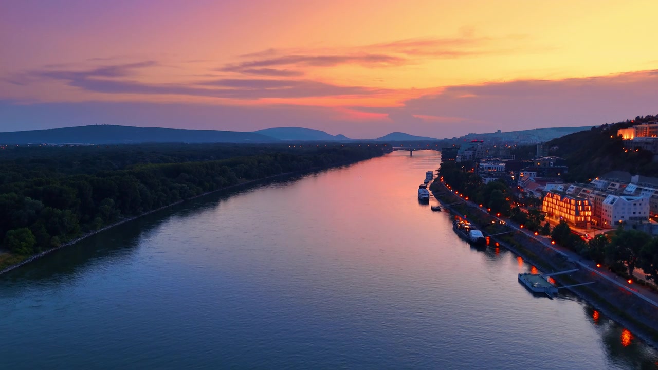 Le Danube au coucher de soleil éclatant à Bratislava, Slovaquie. Vue aérienne de l'eau du fleuve sous un ciel de soirée coloré avec les berges de la ville et des collines lointaines