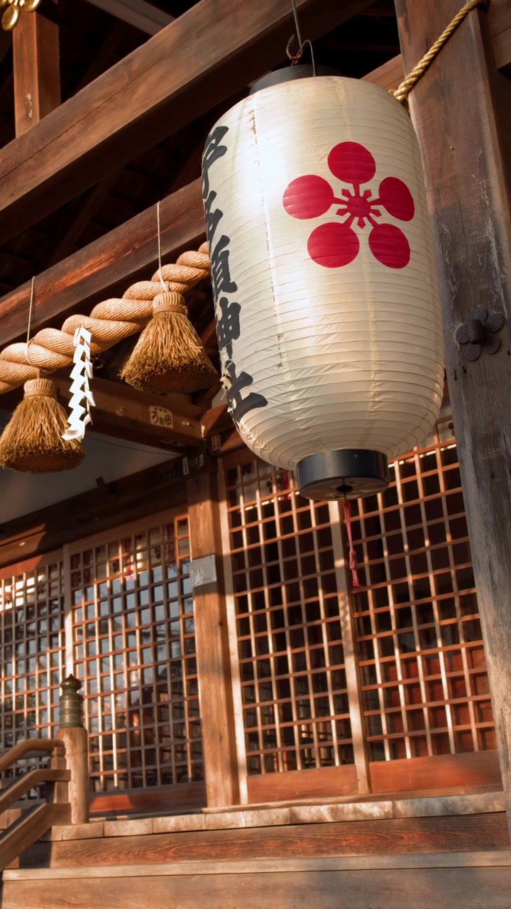 A low angle shot of a white paper lantern hanging from a wooden Shinto shrine