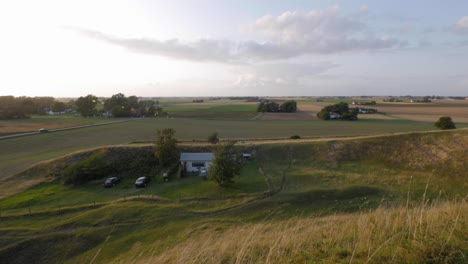 tiny white cottage hidden behind the hills of large countryside fields and trees with two cars, handheld wide shot