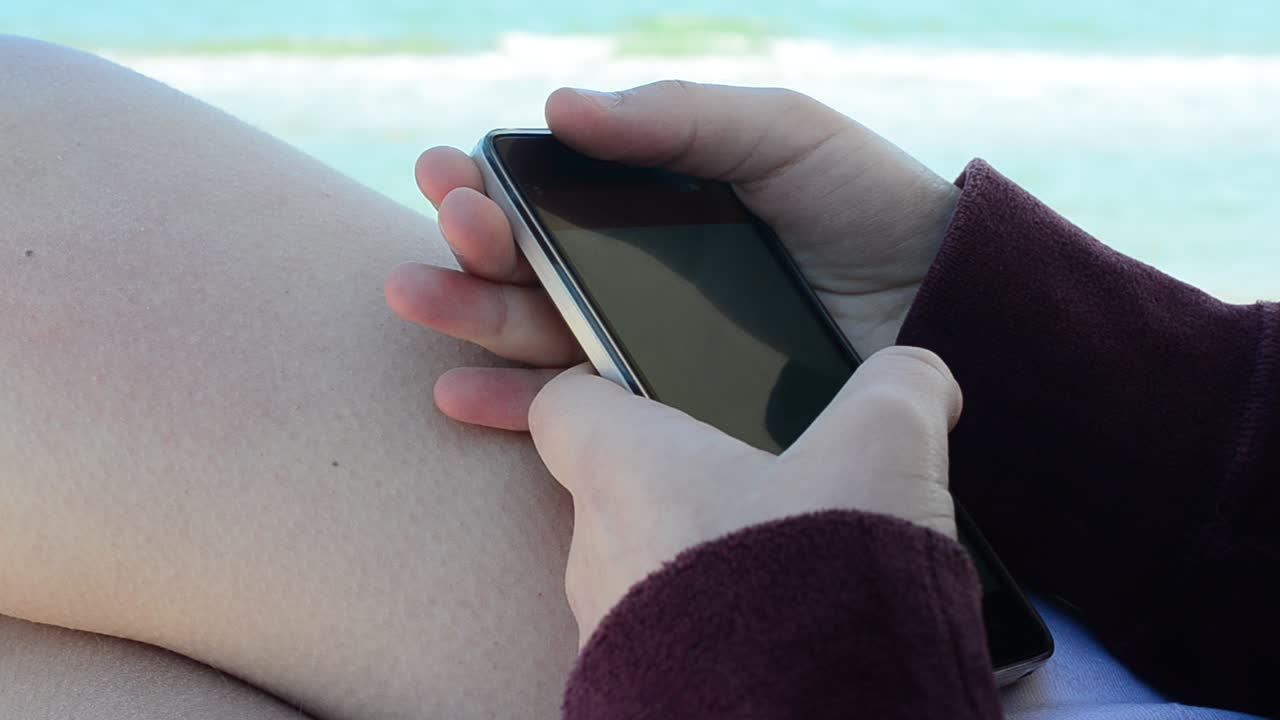 La ragazza con lo smartphone davanti al mare, sulla spiaggia. Scatto sulla spiaggia.