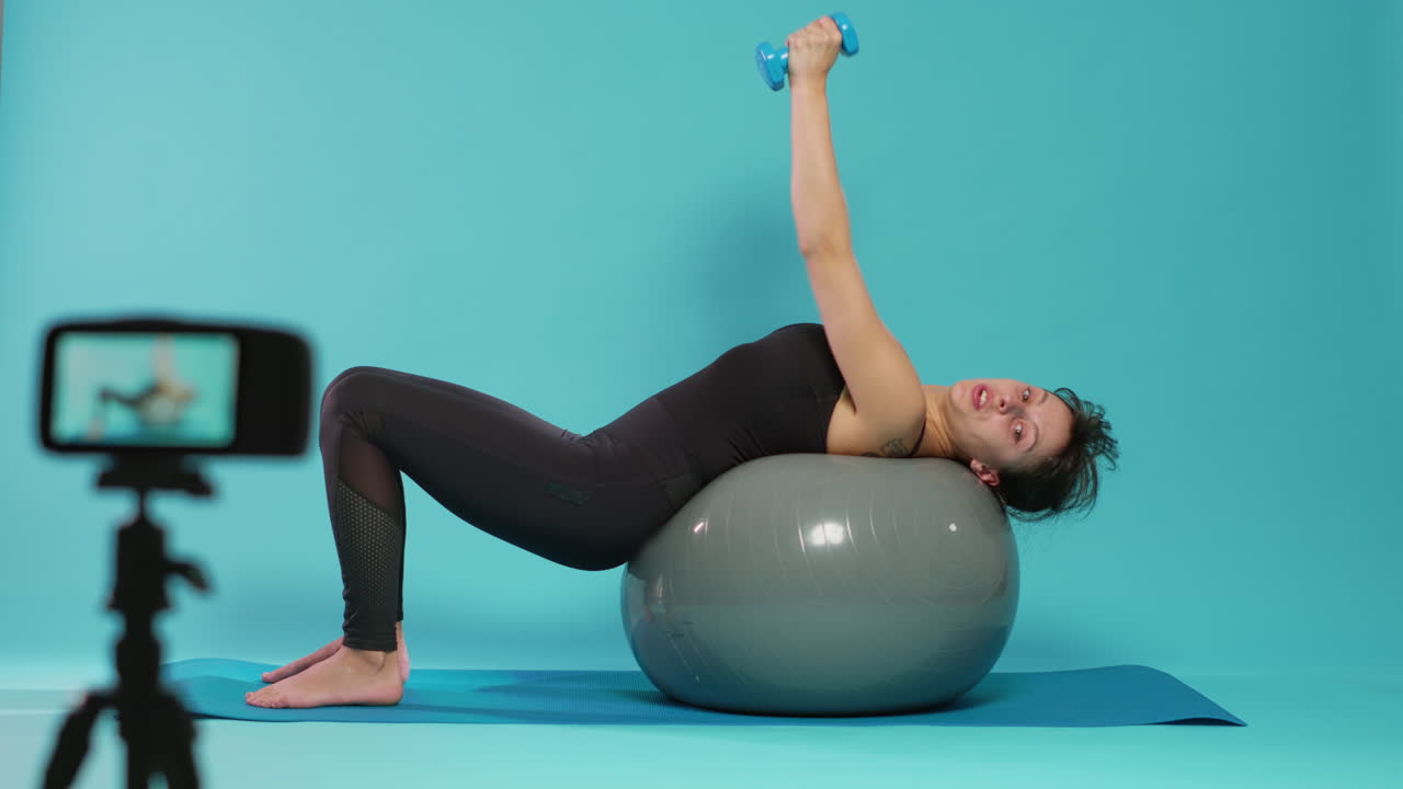 Woman recording workout tutorial with dumbbells and fitness toning ball