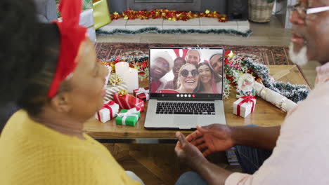 una pareja de ancianos afroamericanos con decoraciones de navidad haciendo una llamada de video con diversos amigos
