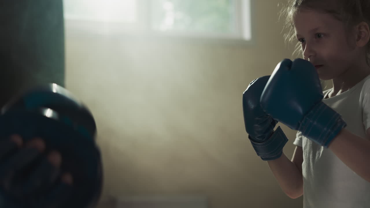 Little kid punches pads on trainer hands in gym. Diligent martial arts young student strikes instructor in sports club slow motion. Training sparring