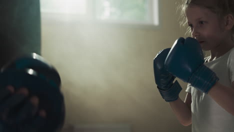 little kid punches pads on trainer hands in gym. diligent martial arts young student strikes instructor in sports club slow motion. training sparring