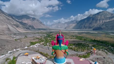 aerial back view of a tall lord budha statue facing towards a majestic mountain valley