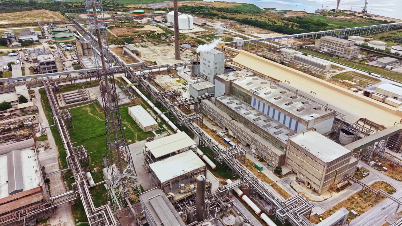 Industrial complex with multiple buildings and pipelines located near water on a clear day