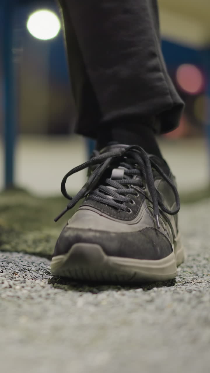 primer plano de las piernas de una persona, centrándose en sus zapatos mientras golpea continuamente su pie en el suelo, el fondo está borroso y débilmente iluminado, con sombras visibles en el suelo