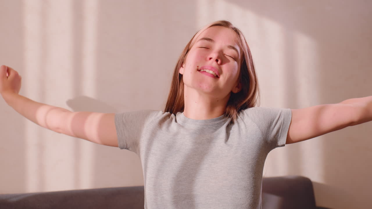 Primer plano de una joven estirándose suavemente tras despertarse. La suave luz del sol proyecta un brillo cálido sobre su rostro mientras se centra en la relajación y la conciencia corporal en un ambiente tranquilo a primera hora de la mañana.