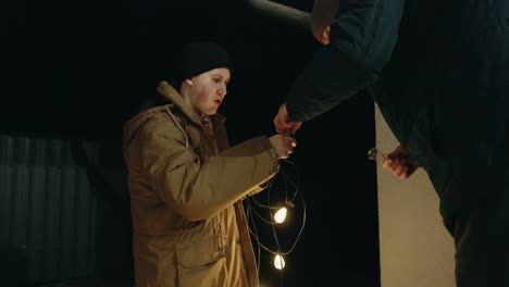 man handing lights to another person at night