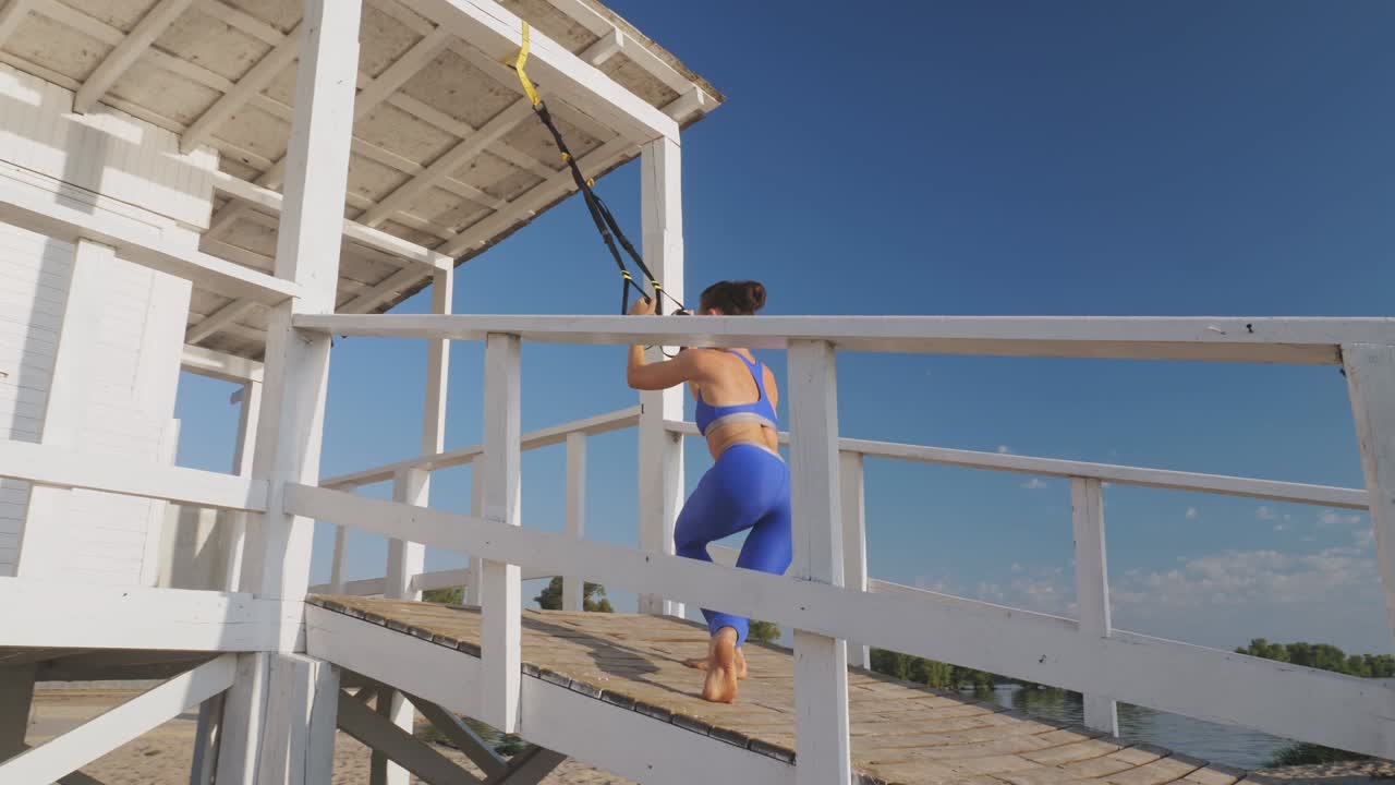 entrenamiento al aire libre. correas de suspensión. entrenamiento con correas. mujer joven atlética está haciendo ejercicios de resistencia de todo el cuerpo usando cuerdas en bucle trx, en la playa durante la puesta o el amanecer. entrenamiento de fitness al aire abierto. concepto de estilo de vida saludable. deporte matutino