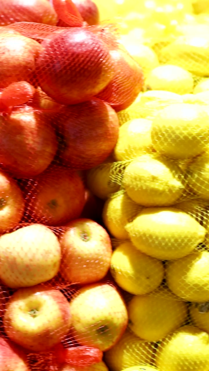 Felgekleurde appels en citroenen gestapeld in netzakken onder warme verlichting in een supermarktomgeving.