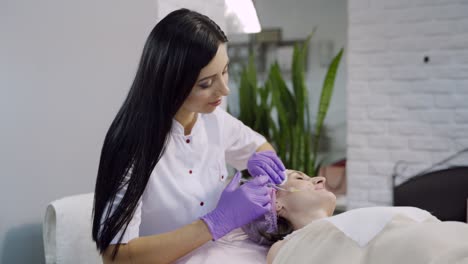a beautician makes biorevitalization on the client's face in the beauty salon on the background of a gray interior of the room.