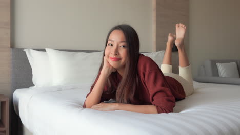 a calm young asian woman lying down on her hotel double bed