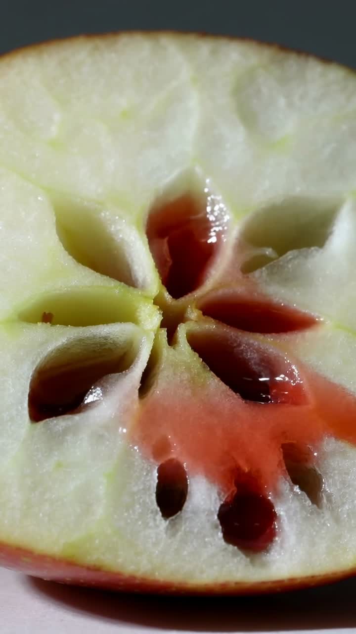 Video verticale: Mela tagliata a metà, sciroppo rosso che scende, si raccoglie nel torsolo e macchia la polpa, cibo.