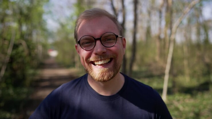 Uomo caucasico bello ed entusiasta con gli occhiali che ride, primo piano nella natura.