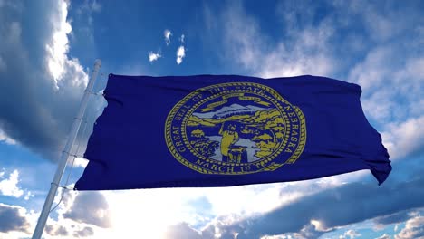 la bandera de nebraska en un asta de bandera ondeando en el viento, fondo de cielo azul. 4k