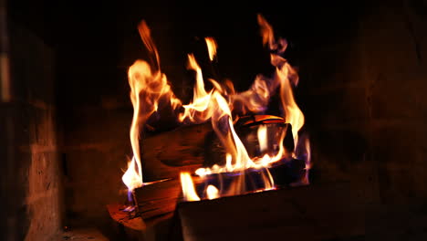firewood burning slowly with sparks. wooden logs in flame inside the fireplace. detailed hot fire in the brickwork fireplace. cozy atmosphere.