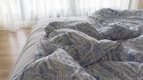 unmade bed with blue and white patterned sheets