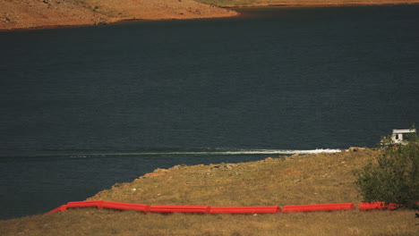 Barco-Que-Viaja-En-El-Lago-Cerca-De-La-Represa-De-Oroville-Con-Boyas-Rojas-En-La-Hierba,-Caluroso-Día-De-Verano