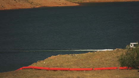 barco que viaja en el lago cerca de la represa de oroville con boyas rojas en la hierba, caluroso día de verano