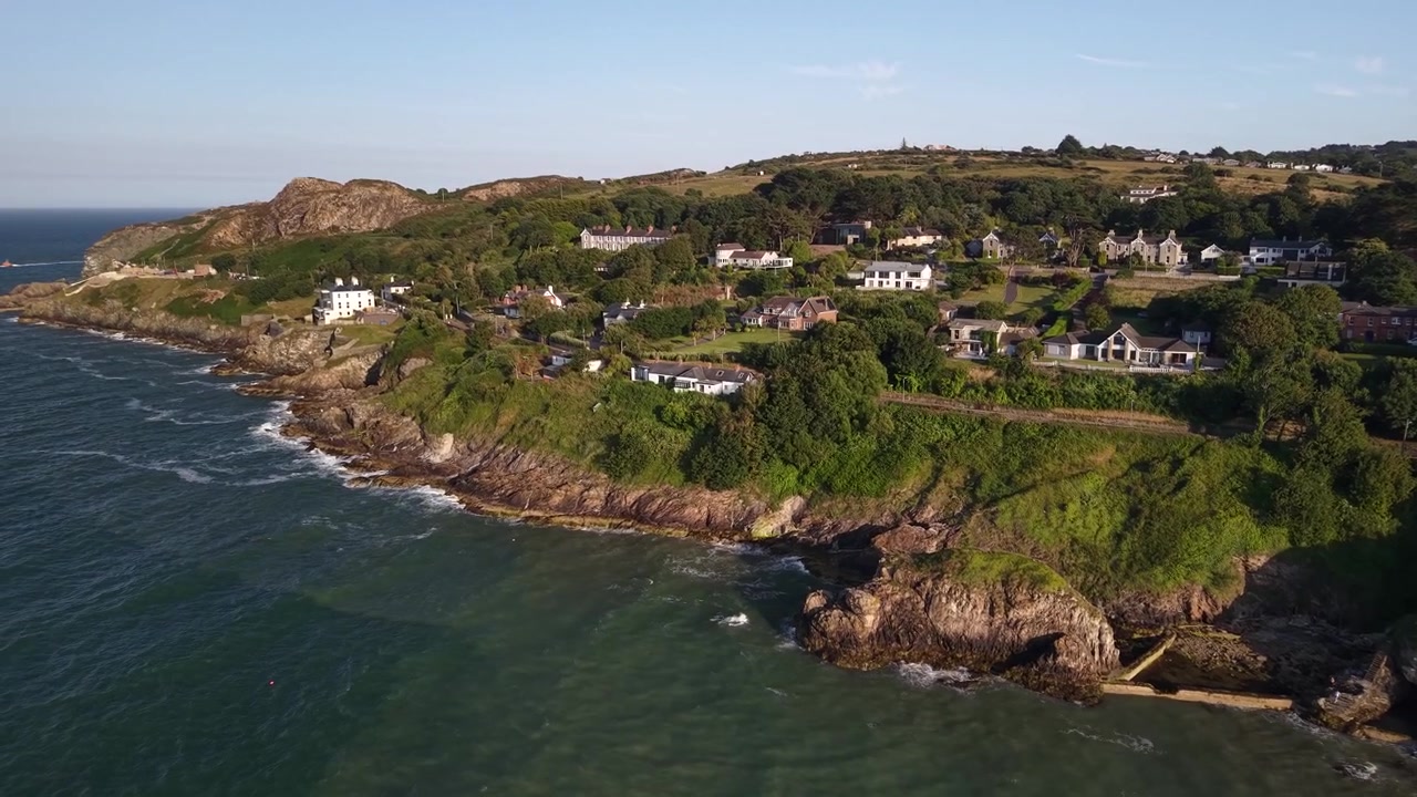 Vista aérea épica da Trilha do Penhasco de Howth e casas costeiras de luxo ao pôr do sol dourado, Irlanda