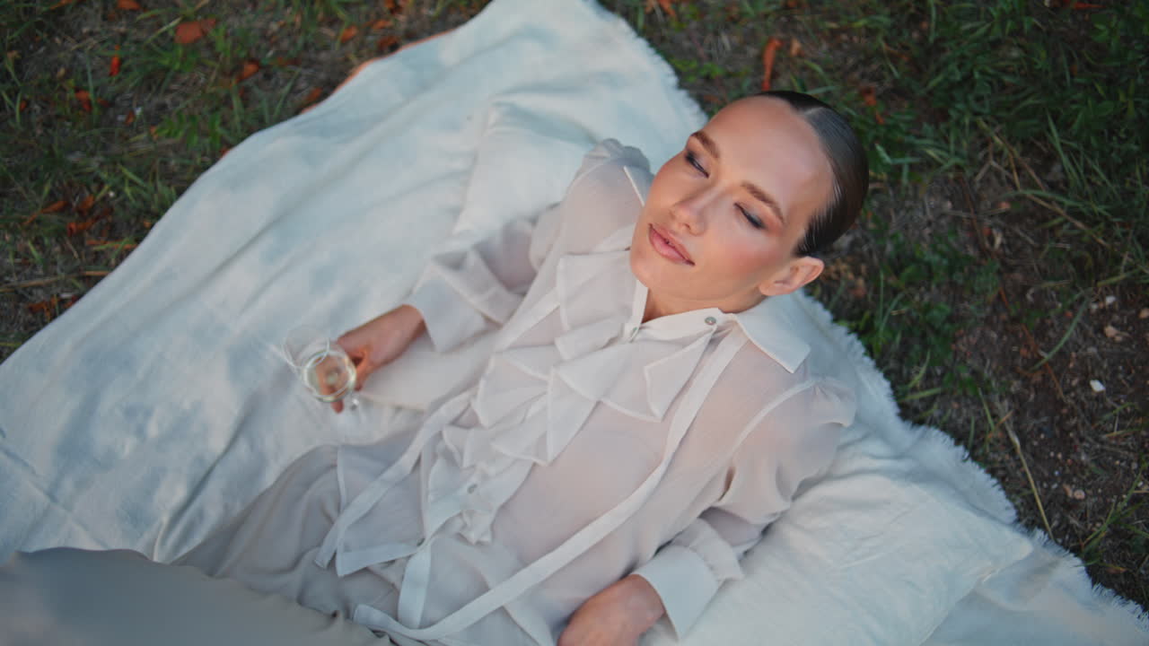 멋진 여자가 피크닉 담요에 누워있는 카메라  뷰를보고 있습니다. 자연을 포즈하는 소녀