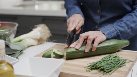 midsection of senior caucasian woman chopping cucumber on kitchen worktop, slow motion