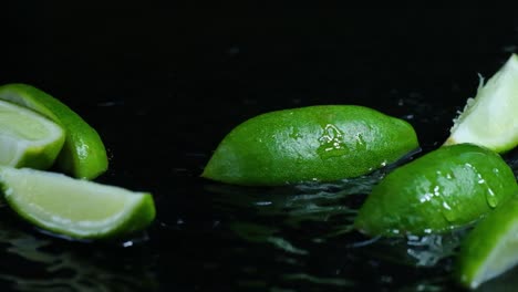 Imágenes-En-Cámara-Lenta-De-4k-De-Limones-Frescos-Que-Caen-En-El-Agua-Y-Salpicaduras:-Las-Limas-De-Limón-En-Rodajas-Caen-Sobre-El-Agua,-Salpicando-Contra-Un-Fondo-Negro