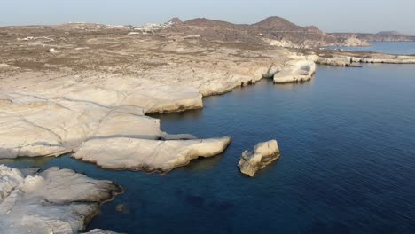 drone view in greece flying over a moon shaped white rock area in milos island at sunrise next to the dark blue sea