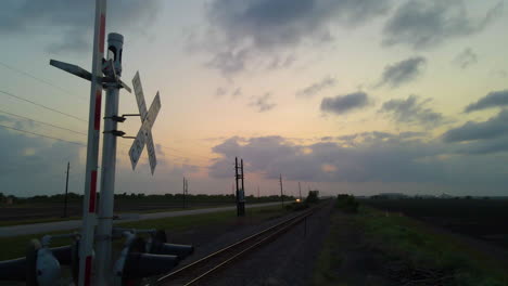 Toma-Aérea-Pasando-El-Letrero-De-Cruce-De-Ferrocarril-Y-Siguiendo-Las-Vías-Al-Atardecer-En-Texas,-U