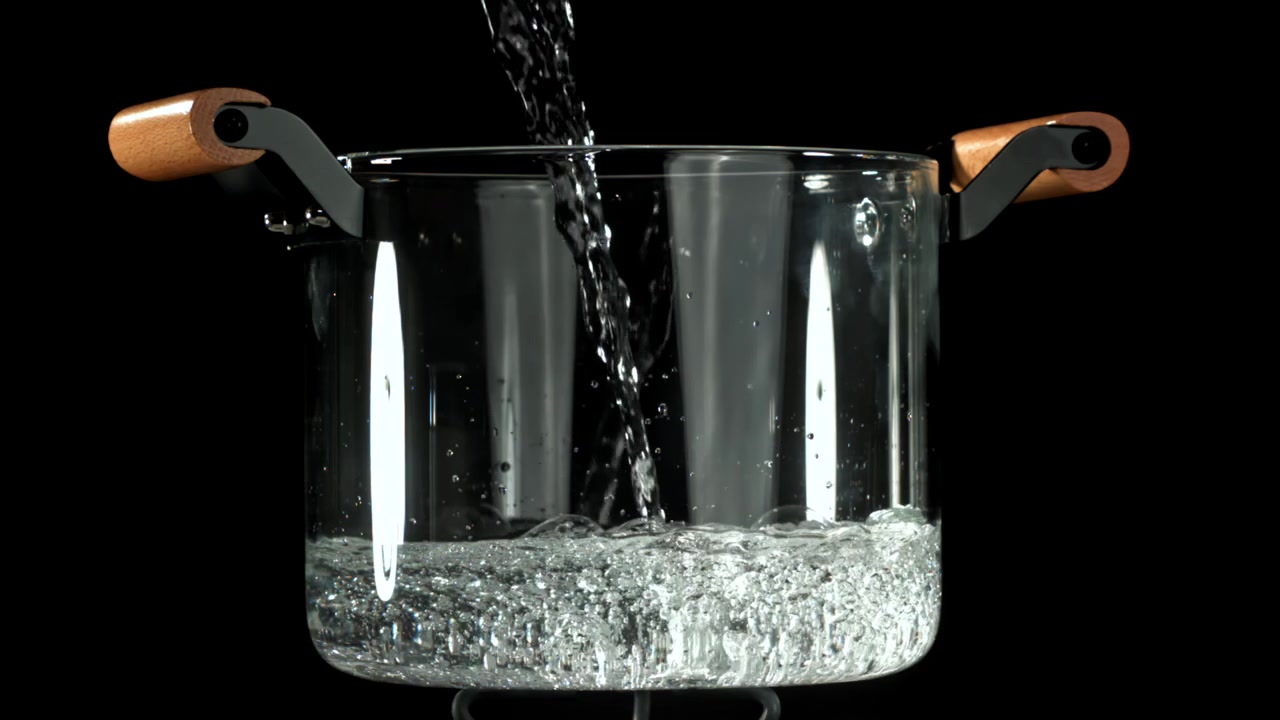 Acqua che si versa al rallentatore in una brocca di vetro trasparente.