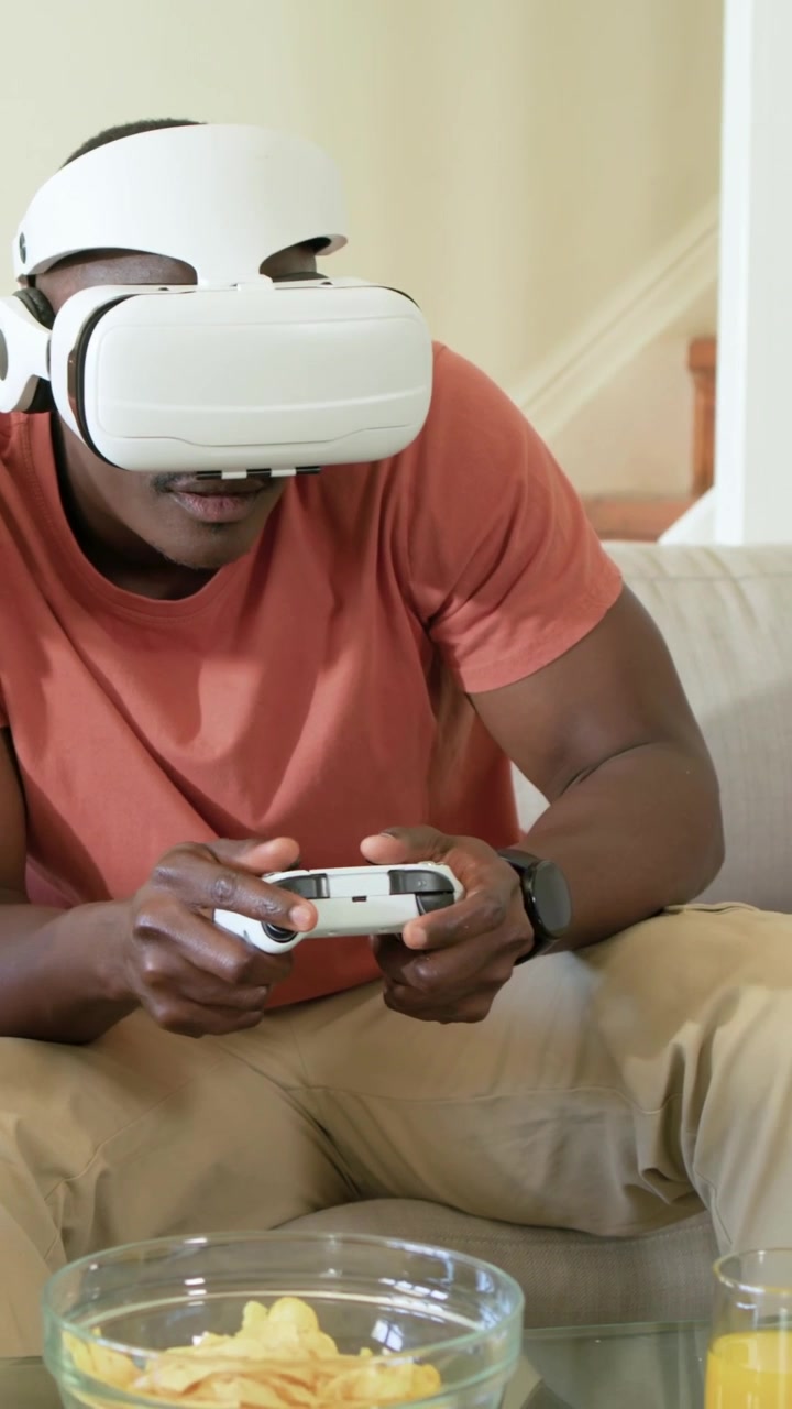 Vertical video: Reacting to game starting, gamer in tee wearing VR, playing with controller on sofa