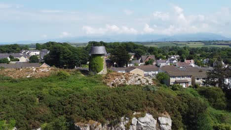 Llangefni-windmill-ivy-covered-hillside-landmark-aerial-dolly-zoom-overlooking-Welsh-Snowdonia-mountains,-Anglesey