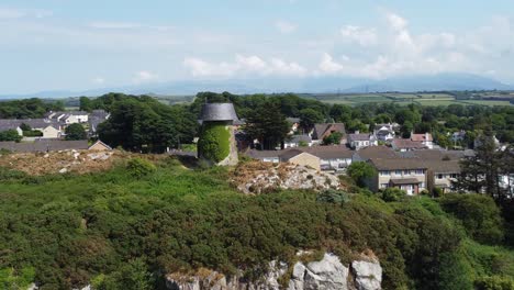 llangefni molino de viento cubierto de hiedra en la ladera de la colina punto de referencia aéreo dolly zoom con vistas a las montañas de snowdonia galés, anglesey