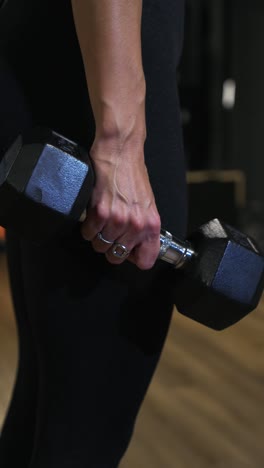 vertical shot of a female athlete holding heavy dumbbells at her side during a workout