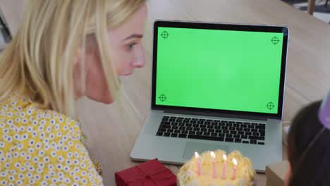 girl blowing cake while having a video chat on laptop at home