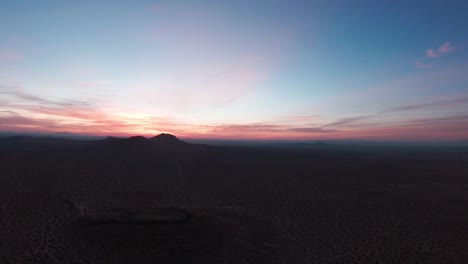 mojave desert at sunrise with a colorful sky above the rugged terrain - aerial pull back view