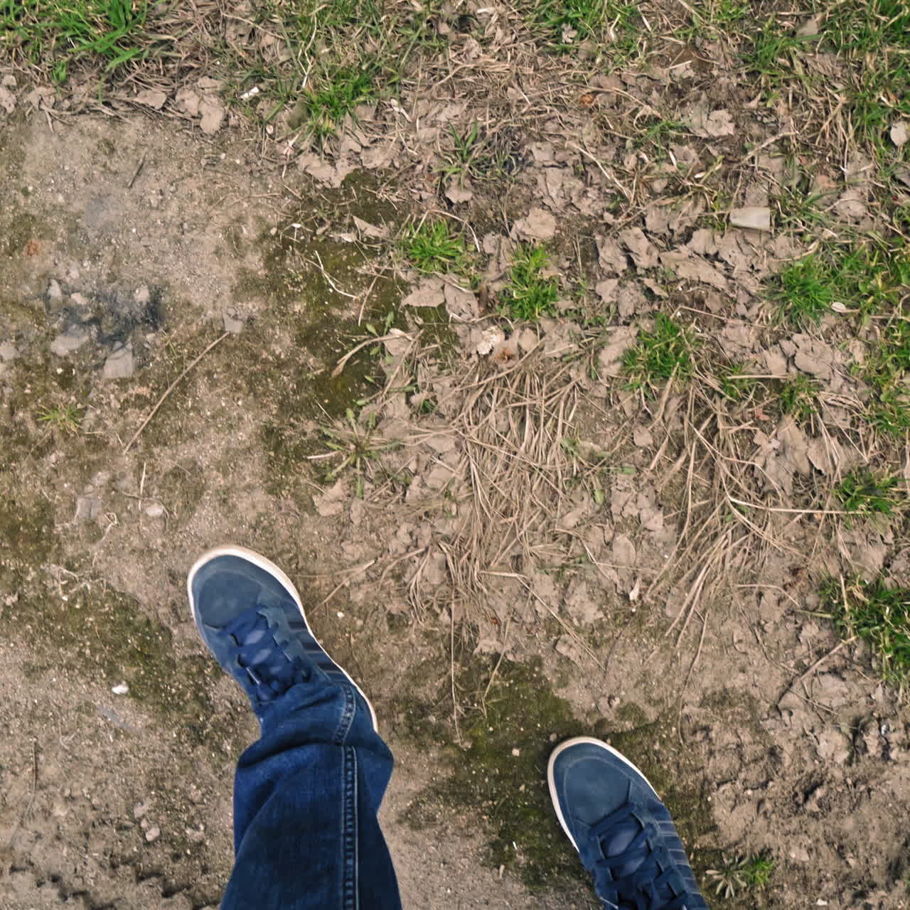 Male's legs going on the ground and a lot of garbage around outdoors. Man in jeans and trainers come into the dirty place with many rubbish on the natural background.