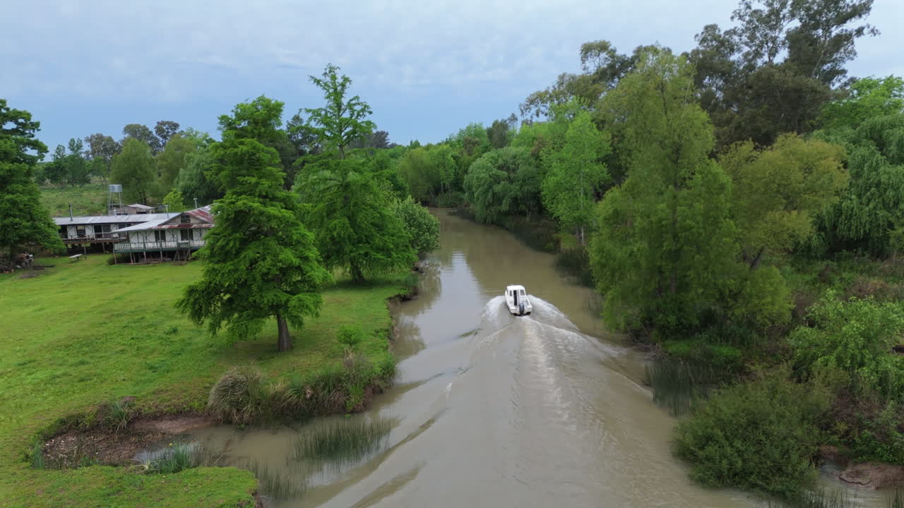 Following aerial view of a motorboat navigating and entering a lush waterway in the Paraná Delta, Argentina.