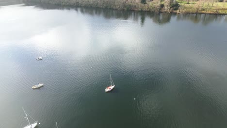 sailboats on dark watered lake, drone flyover