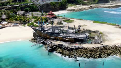 old wooden ship moored on stones in tropical beach of bali, aerial orbit view