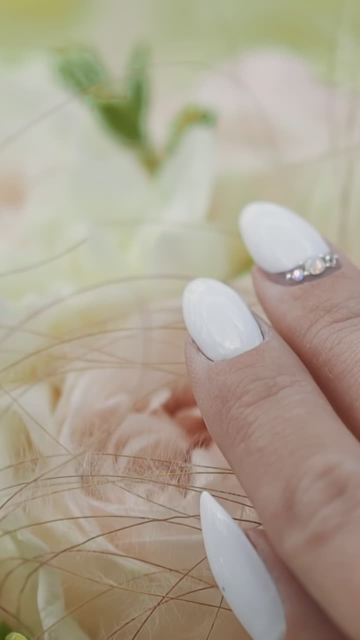 Elegant young bride hand with white designer manicure touches wedding bouquet of roses on blurred background closeup. Marriage and engagement celebration