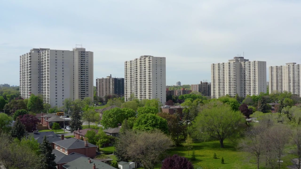 Slow aerial drone movement highlighting clusters of residential apartment towers surrounded by detached homes, mature trees, and landscaped suburban neighborhoods during spring. Ideal for housing, arc