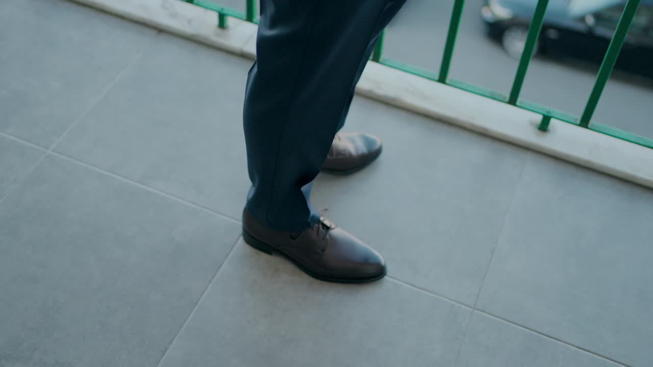 Man in dress shoes standing on a tiled balcony with green railing