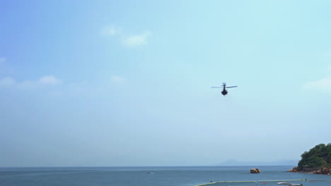 a medical service rescue helicopter takes off from an island and flies away over the ocean under a clear blue sky