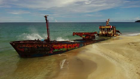 Graffiti-covers-an-abandoned-shipwreck-buried-in-the-beach,-Manzanillo,-Costa-Rica,-aerial-orbit