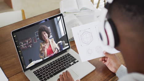 estudiante universitario afroamericano que sostiene notas mientras hace una videollamada en una computadora portátil en casa