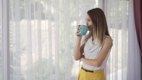 la mujer que bebe café está en casa junto a la ventana.